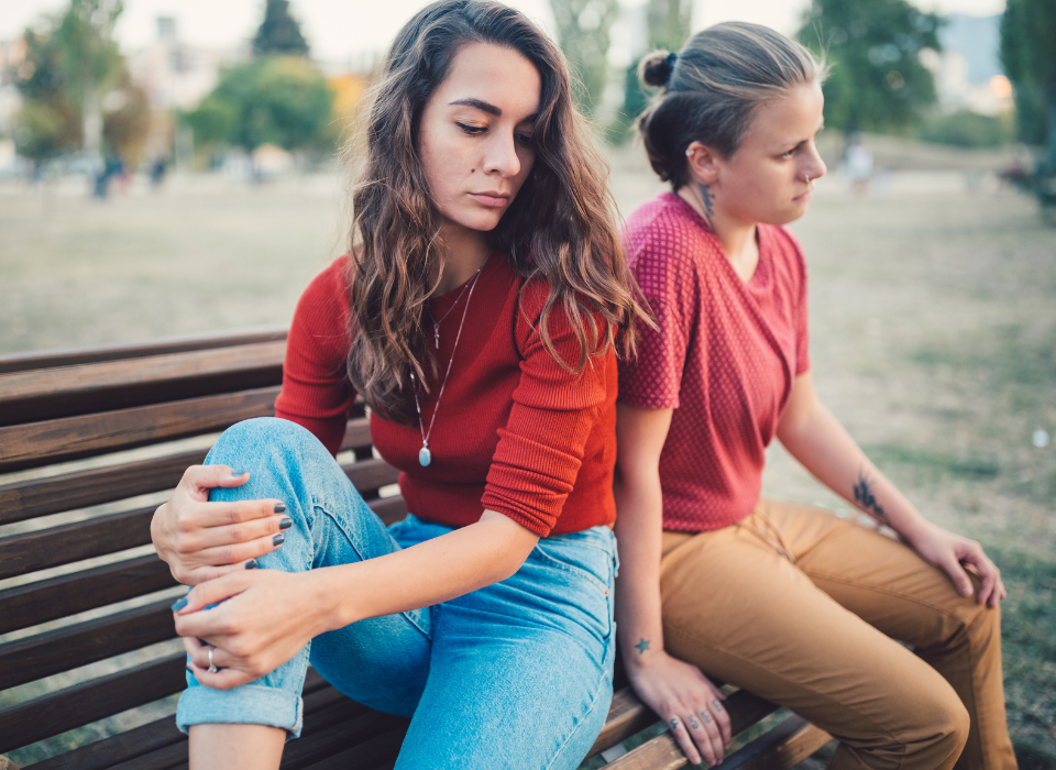 Two teens sitting apart on a park bench, appearing distant and emotionally disconnected.