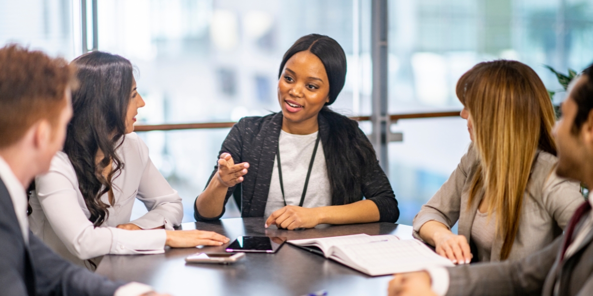 A woman exemplifying executive presence for women by speaking assertively and commanding attention while leading a focused discussion with colleagues around a conference table.
