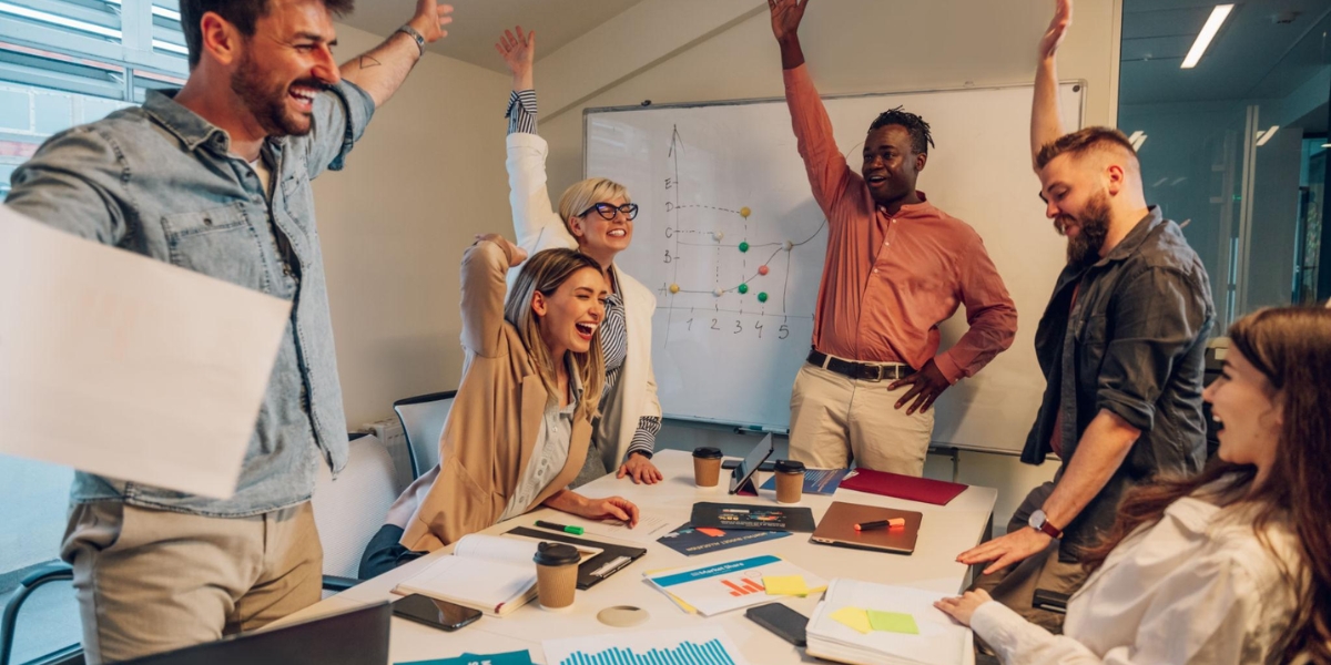 Participative leadership style shown through a diverse team celebrating success together in an office setting, with team members actively contributing ideas and raising hands in agreement.